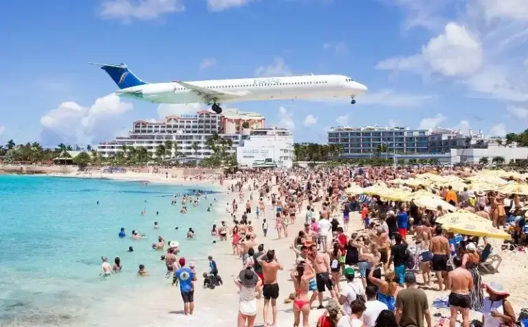 Un avion passe au-dessus des touristes sur la célèbre plage de Maho Beach à Saint-Martin